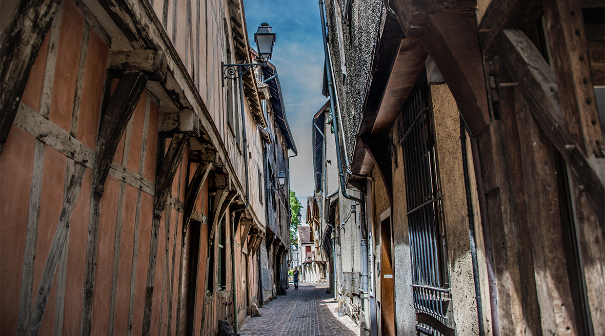 Very old half-timbered buildings on either side of a very narrow lane lean close to each other